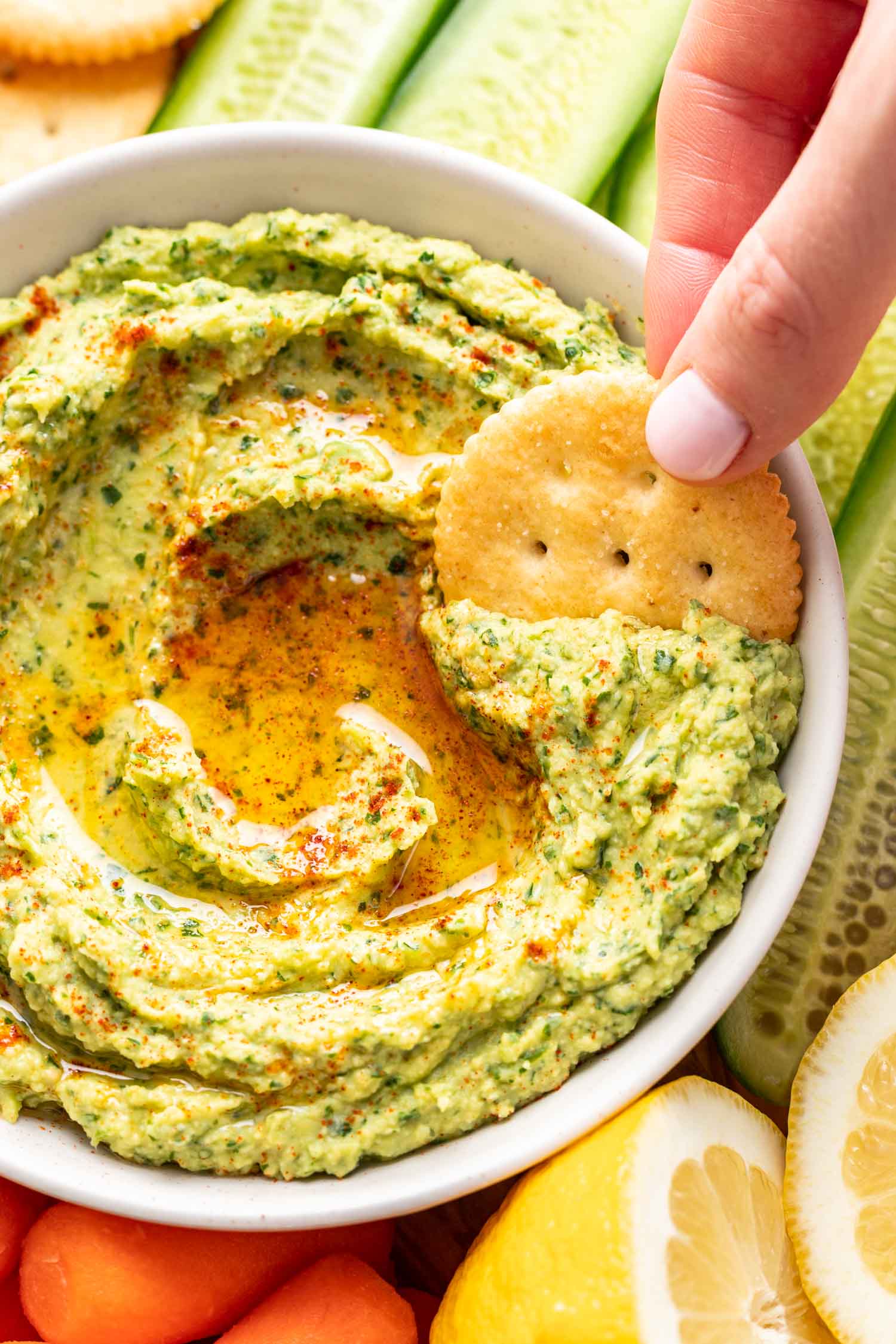 a cracker dipping into herb avocado dip