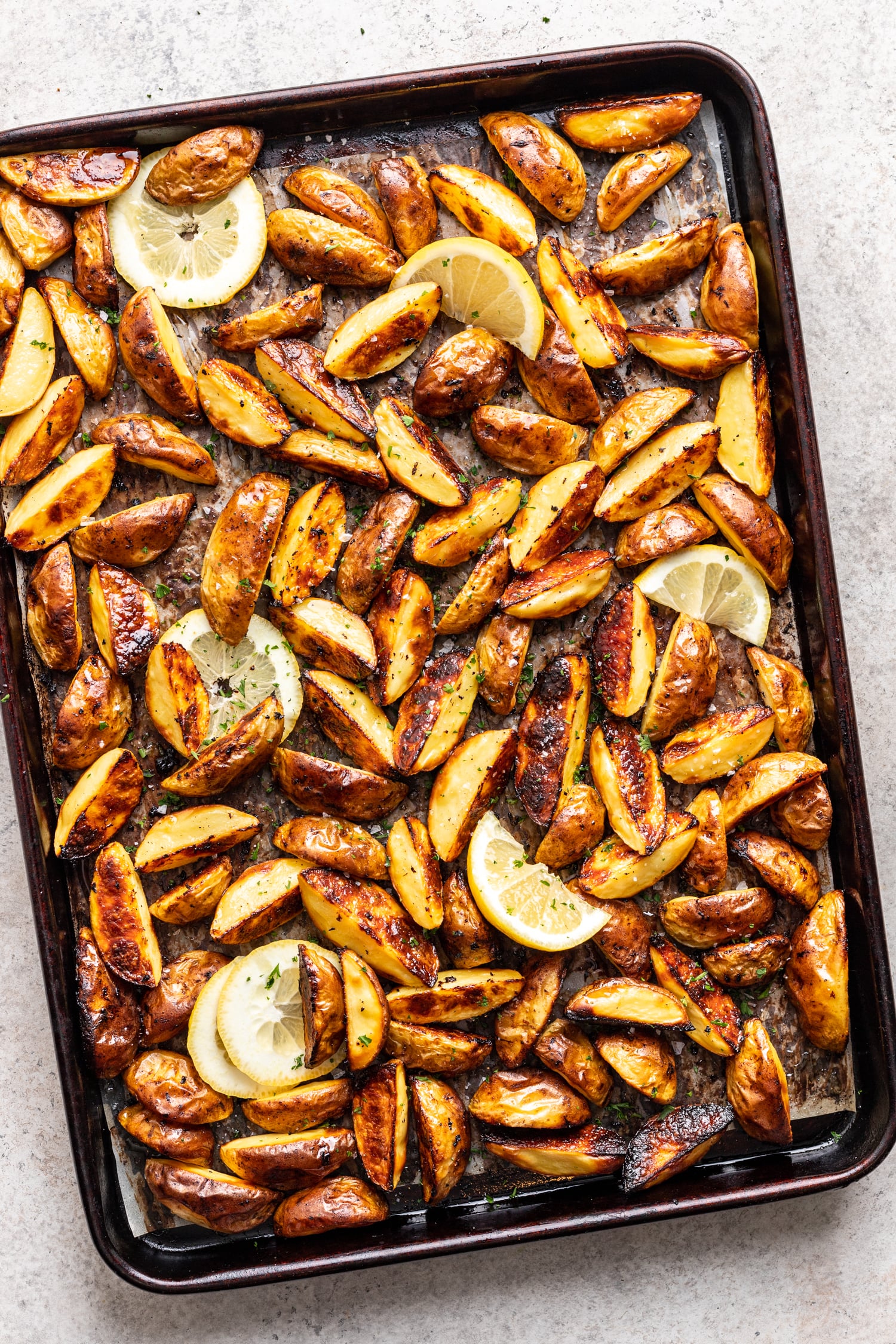 roasted potatoes on a sheet pan with lemon wedges