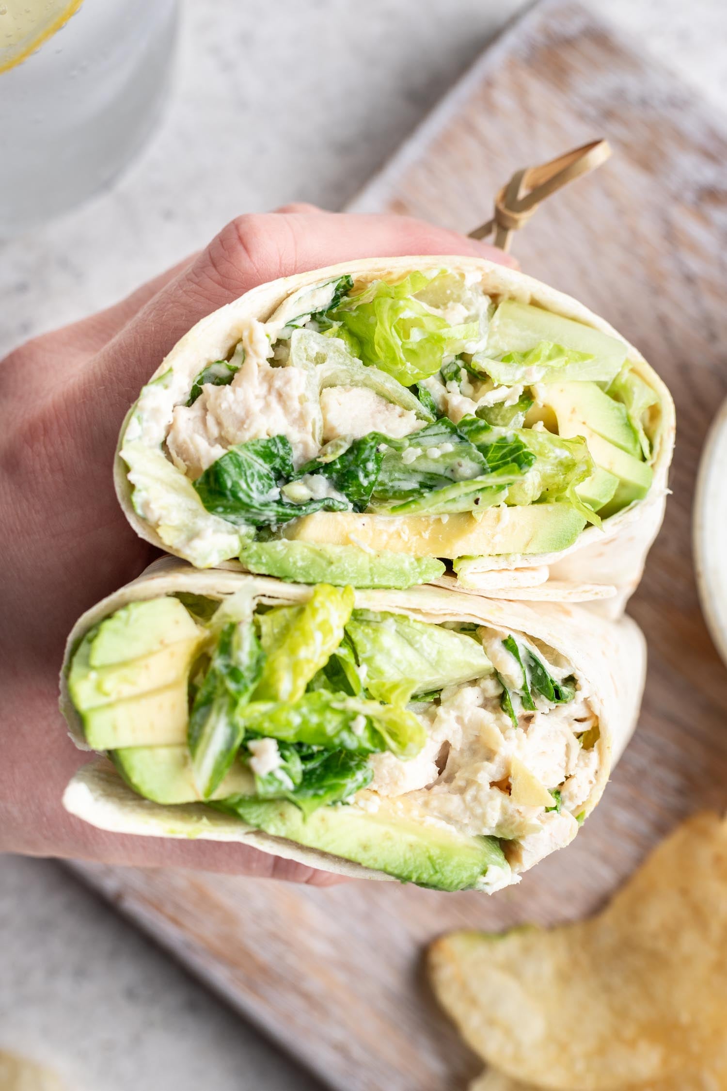 a hand holding a chicken caesar wrap cut in half and stacked with a toothpick