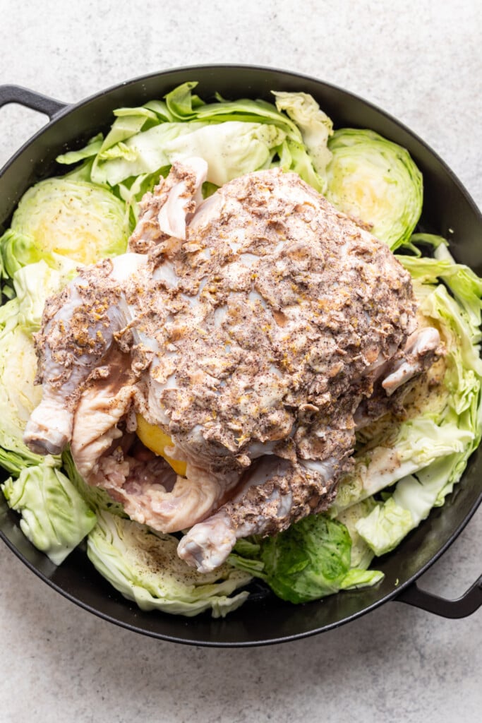 whole raw chicken covered with lemon butter on a bed of cabbage