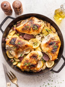 cast iron skillet with cooked chicken, potatoes and lemon
