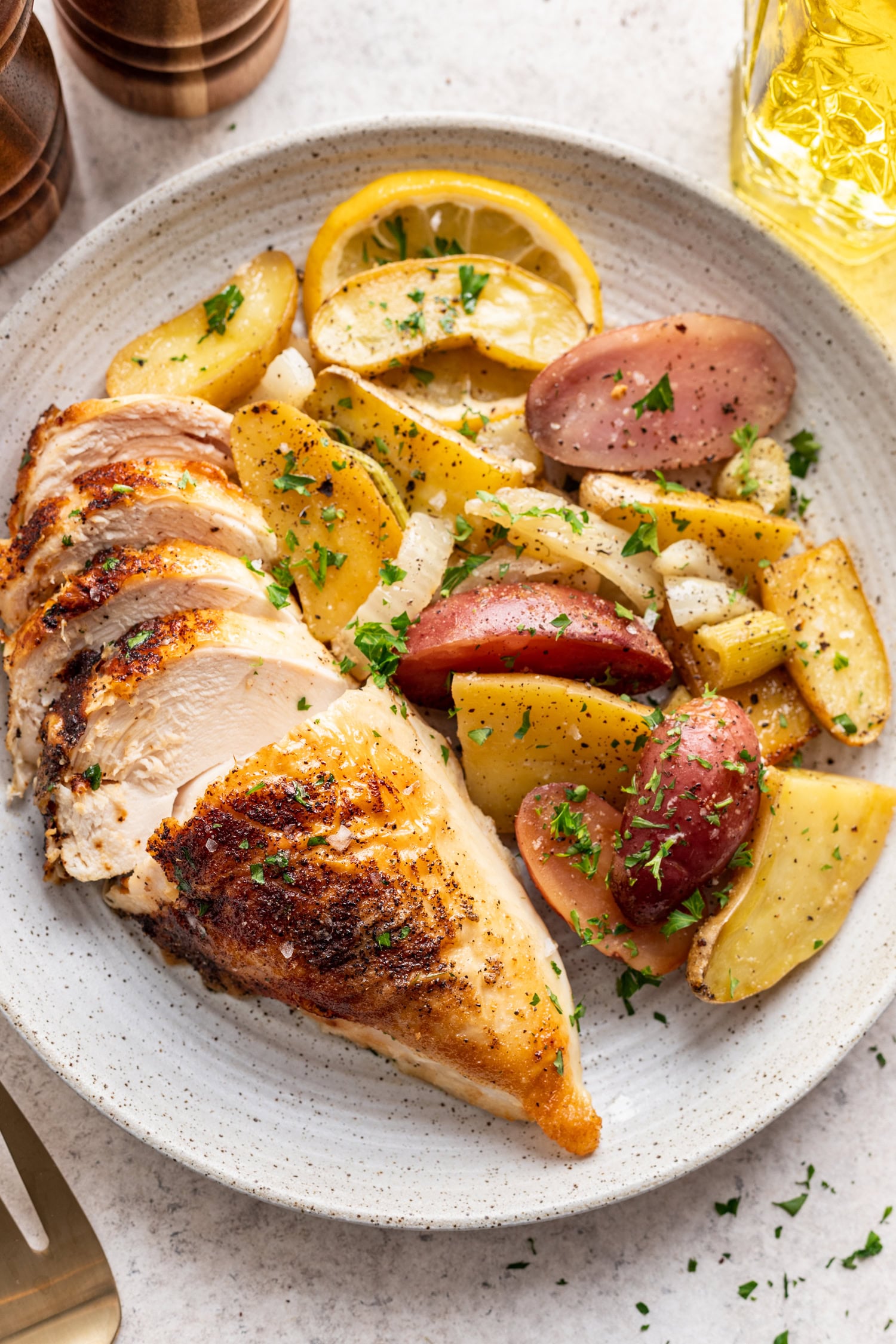 sliced chicken breast with crispy skin and a side of potatoes and fennel on a white plate