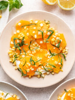 sliced oranges on a white plate with fresh corn and chopped basil