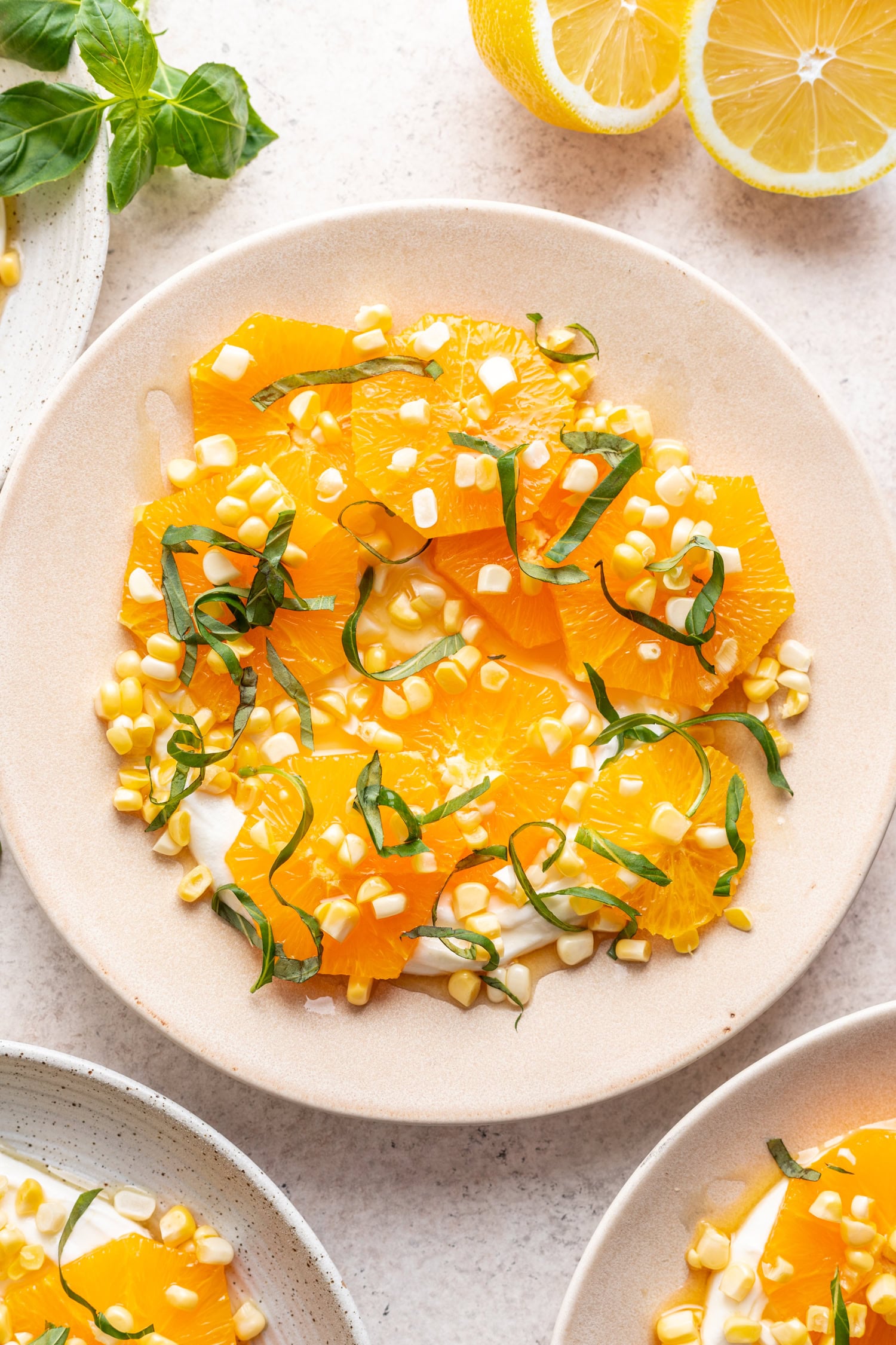 sliced oranges on a white plate with fresh corn and chopped basil