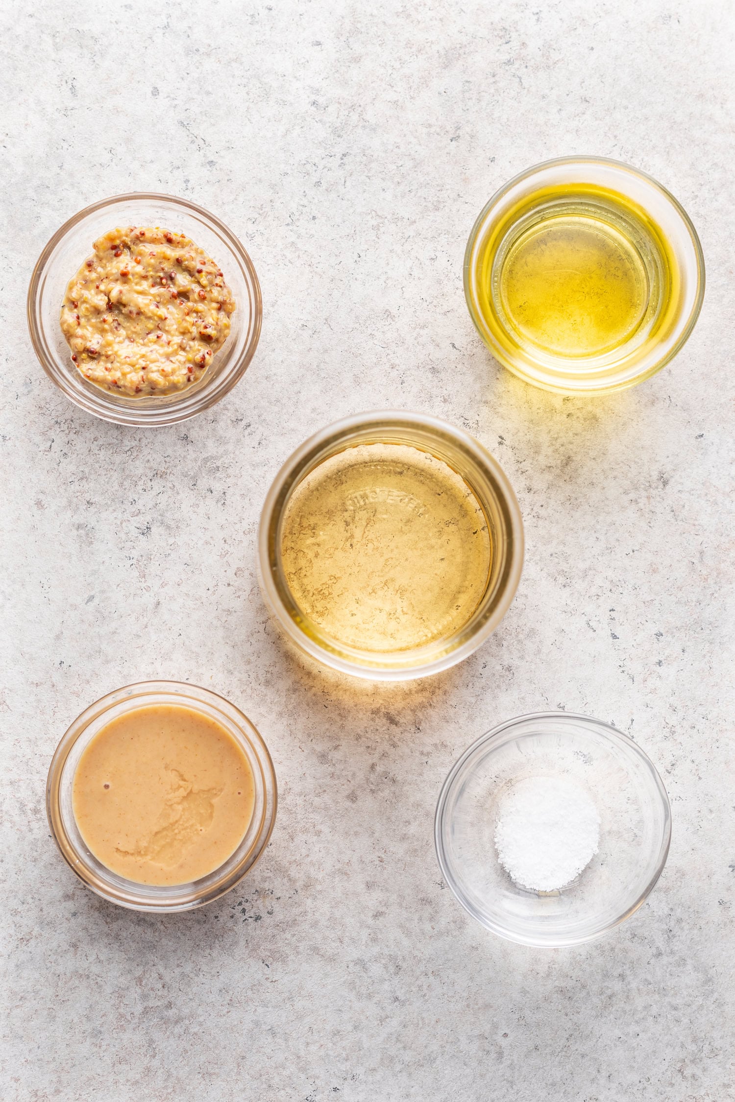bowls of ingredients on a grey background. Oil, tahini, mustard and balsamic vinegar