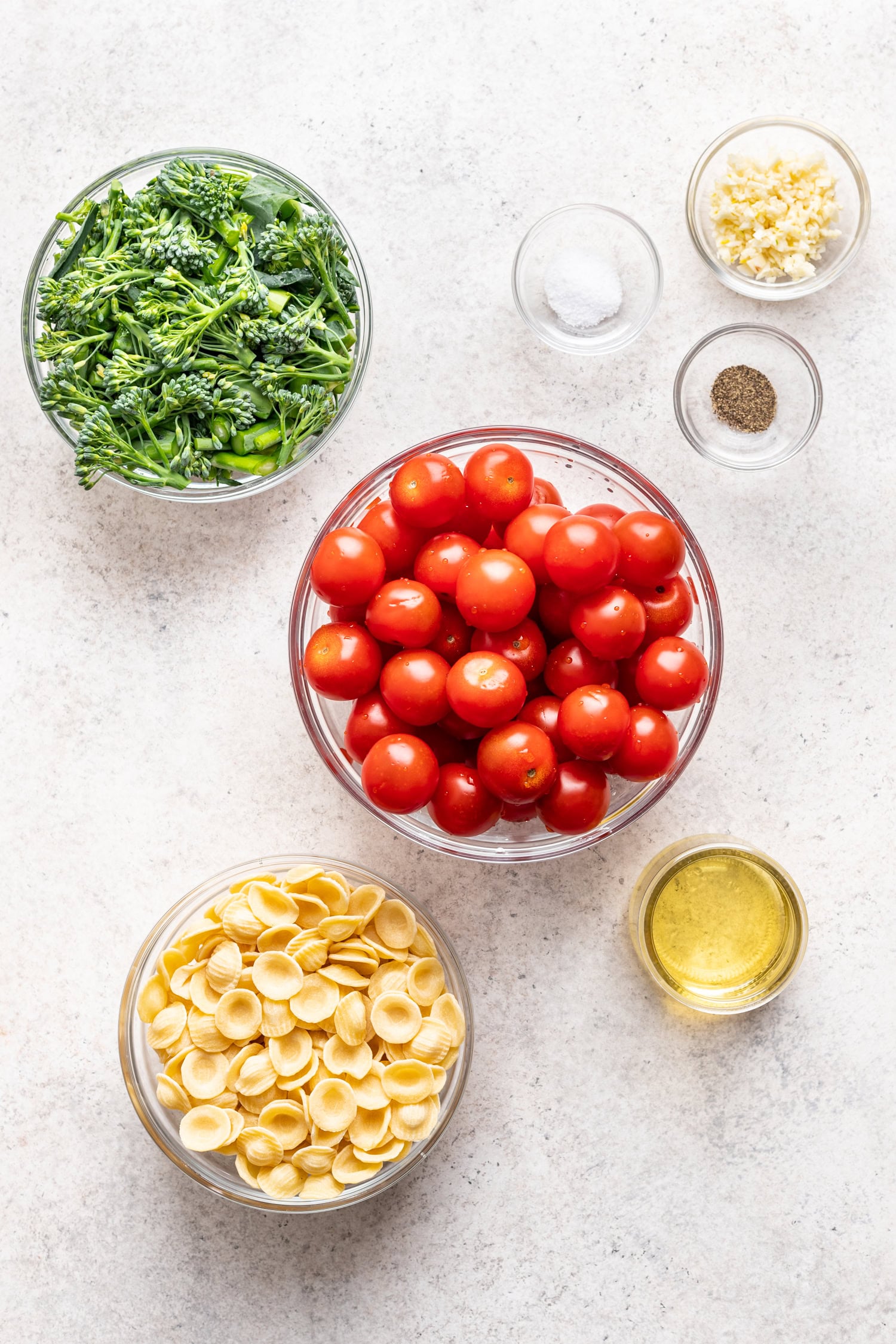 bowls of ingredients like cherry tomatoes, broccolini, pasta, oil and spices