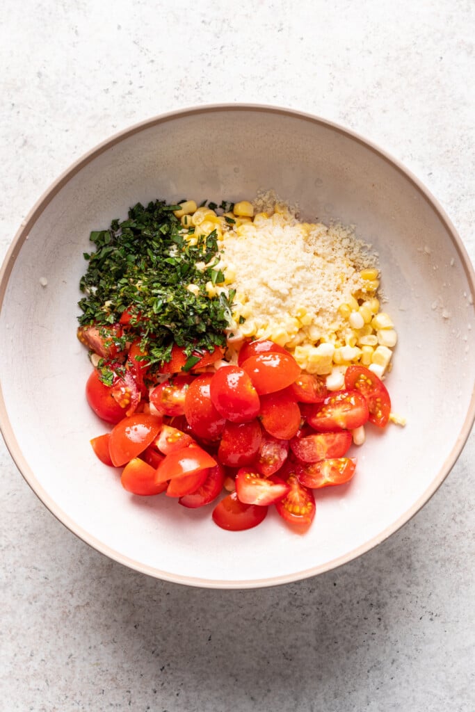white bowl with tomatoes, corn, parmesan and fresh herbs