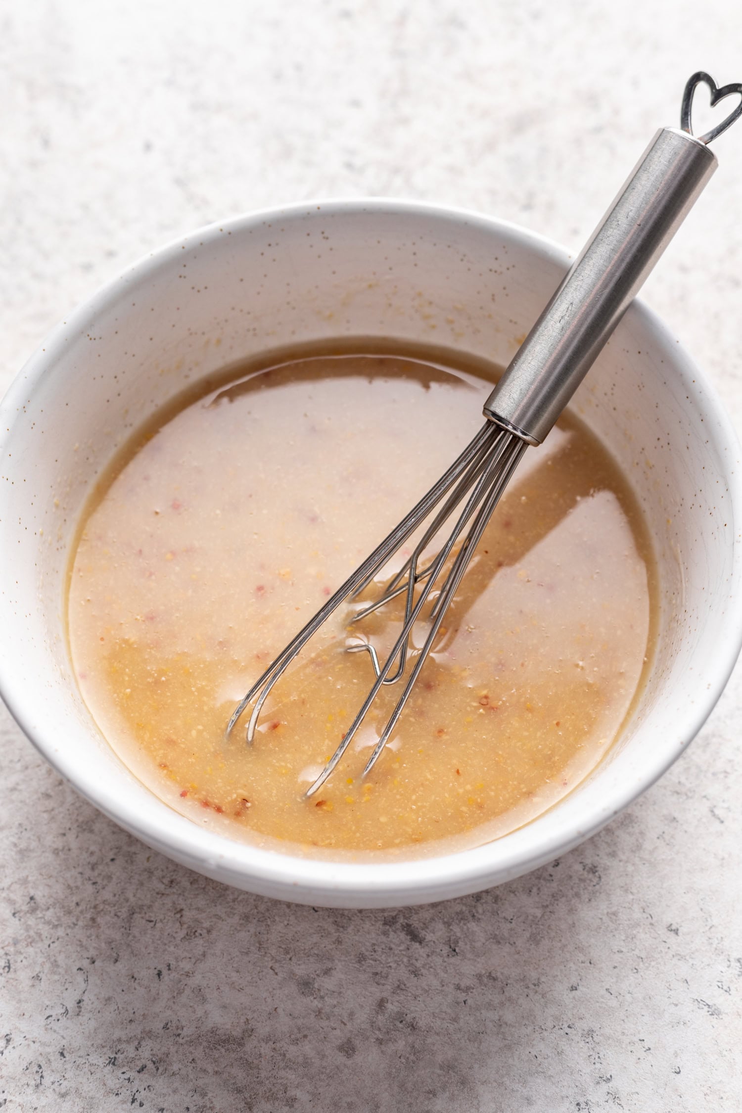 white bowl with tahini mustard dressing with a whisk shown at a 45 degree angle