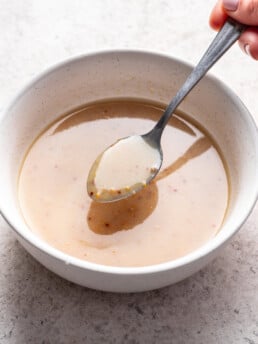a spoon scooping some dressing from a white bowl