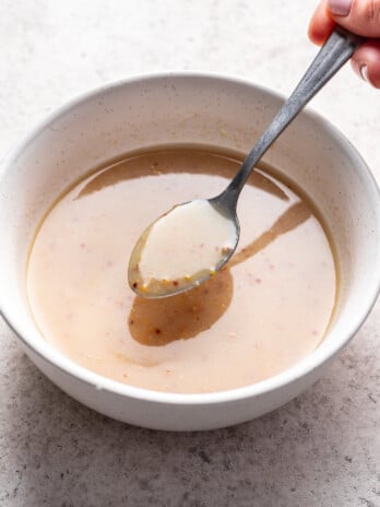 a spoon scooping some dressing from a white bowl