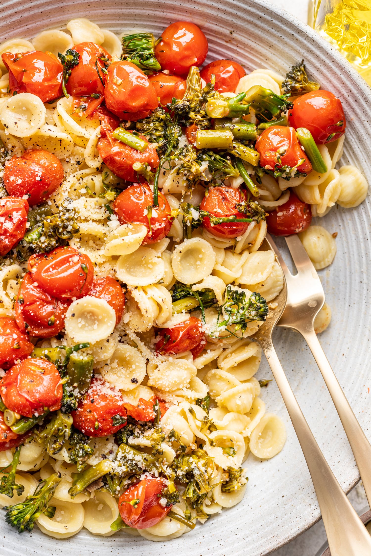 serving spoons in a bowl of pasta with roast tomatoes and broccolini