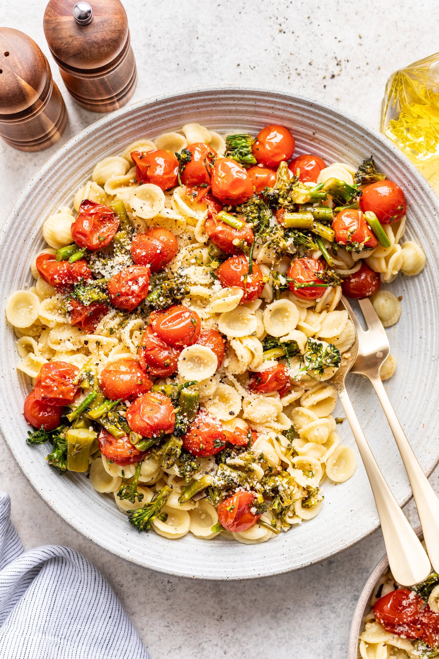 bowl of roasted tomatoes and broccolini over pasta with serving spoons