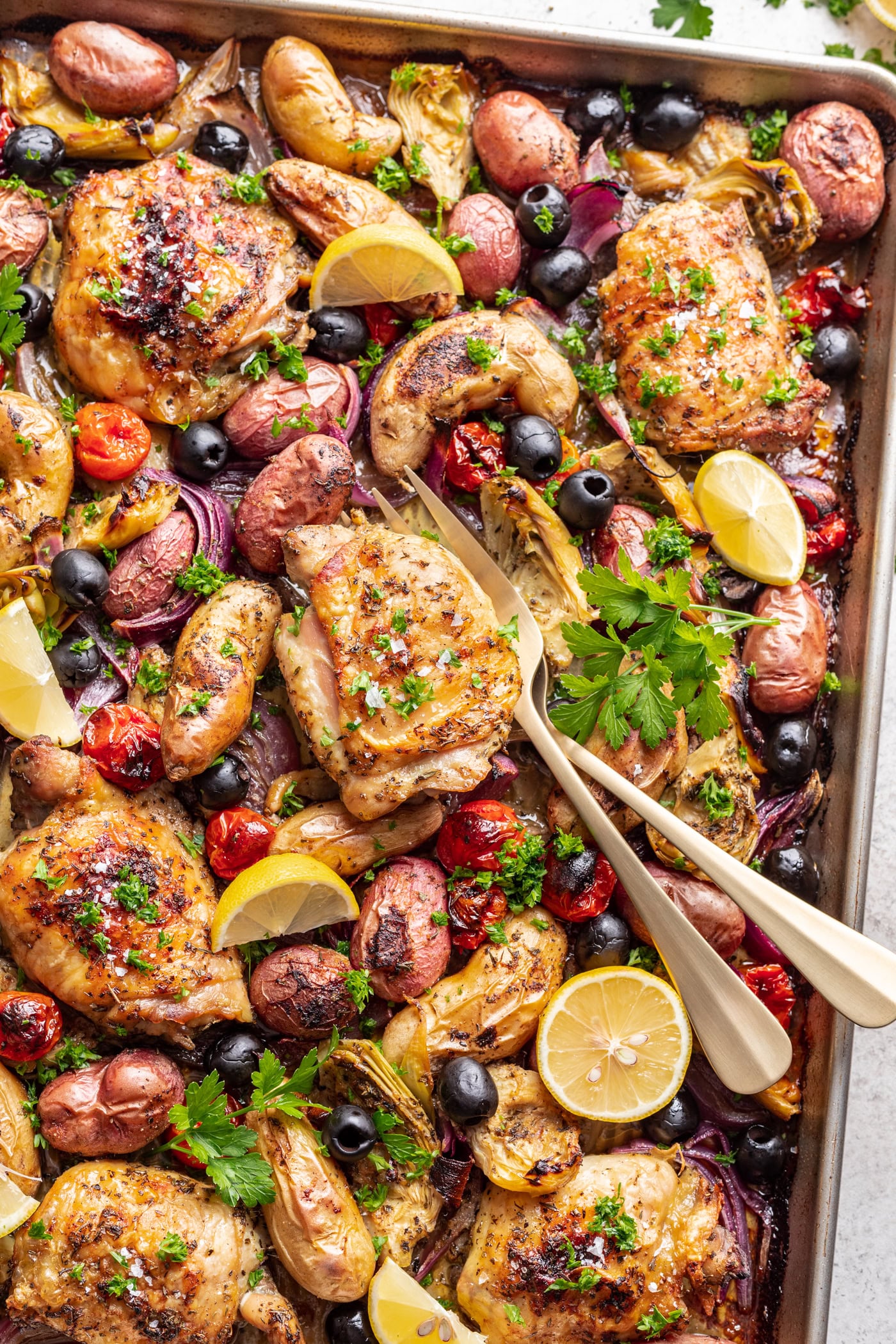 roasted chicken thigh with potatoes, olives and tomatoes and two serving forks