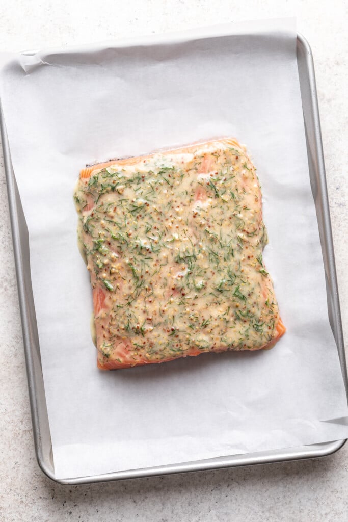 a piece of salmon on a parchment lined baking sheet with dill sauce on top