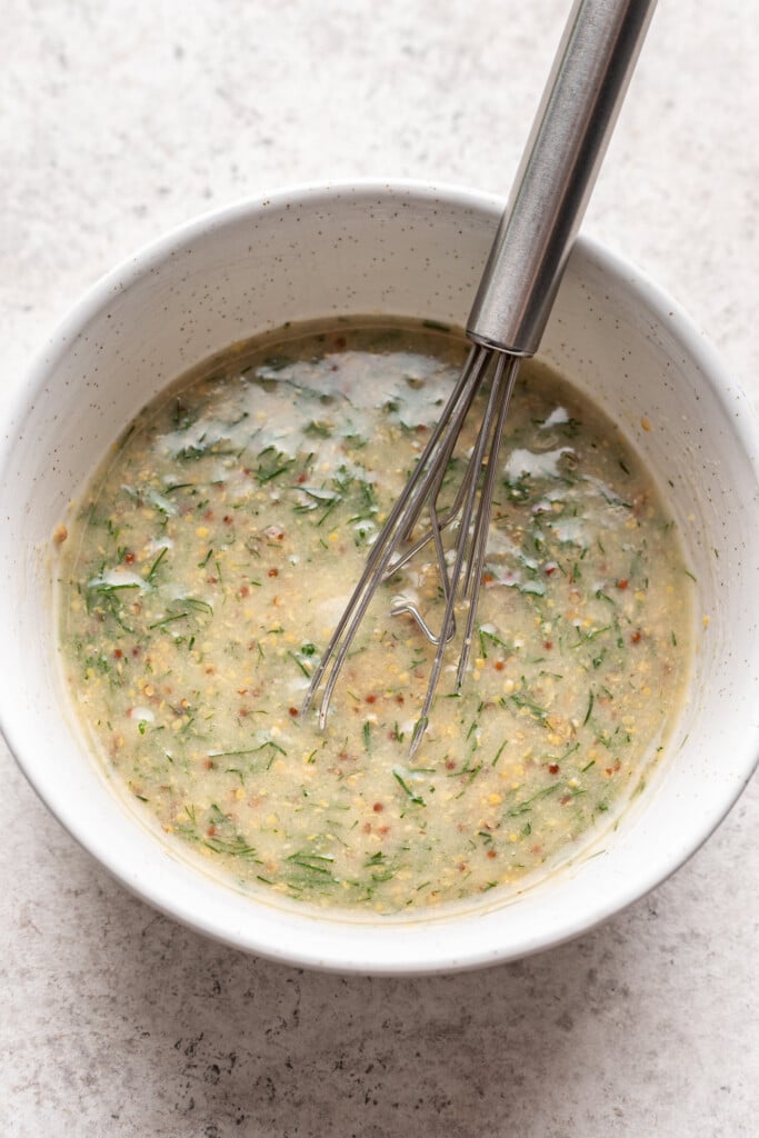 mustard dill sauce in a white bowl with a whisk