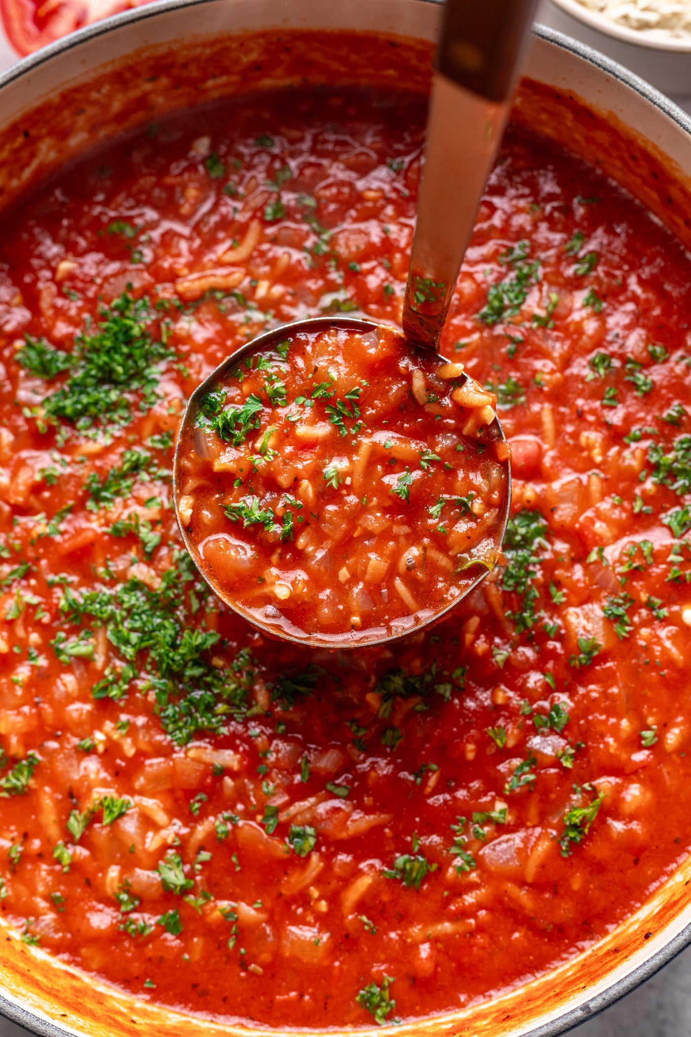 ladle scooping out tomato rice soup in a pot