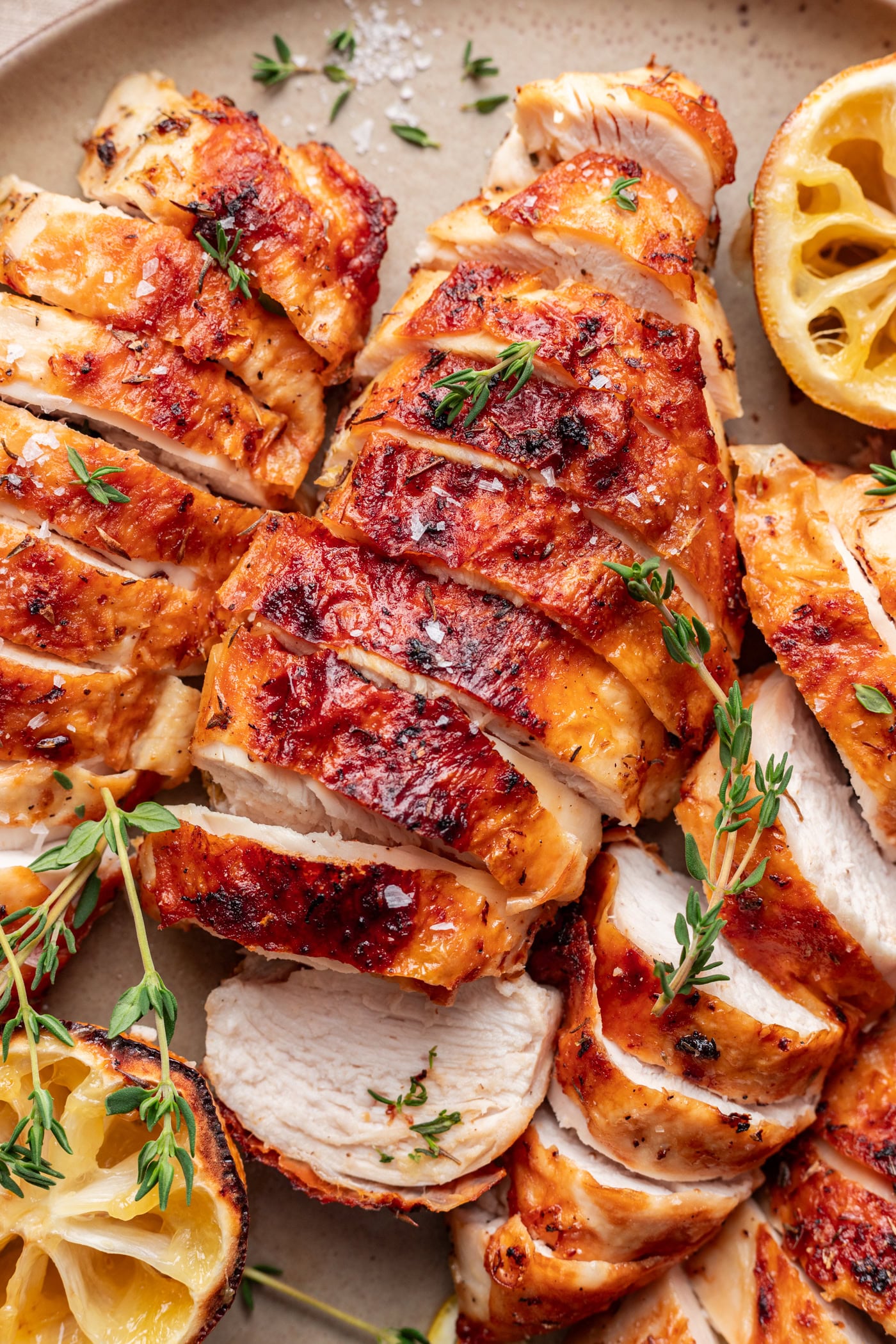 Sliced, golden-brown lemon roasted chicken breast garnished with fresh thyme, served on a plate with halved, grilled lemons and a sprinkle of coarse salt.