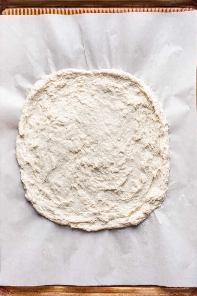 flattened cottage cheese pizza dough on parchment paper