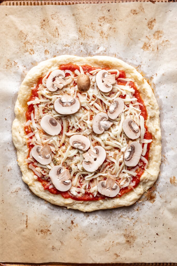 A pizza with cheese and mushrooms on a parchment paper