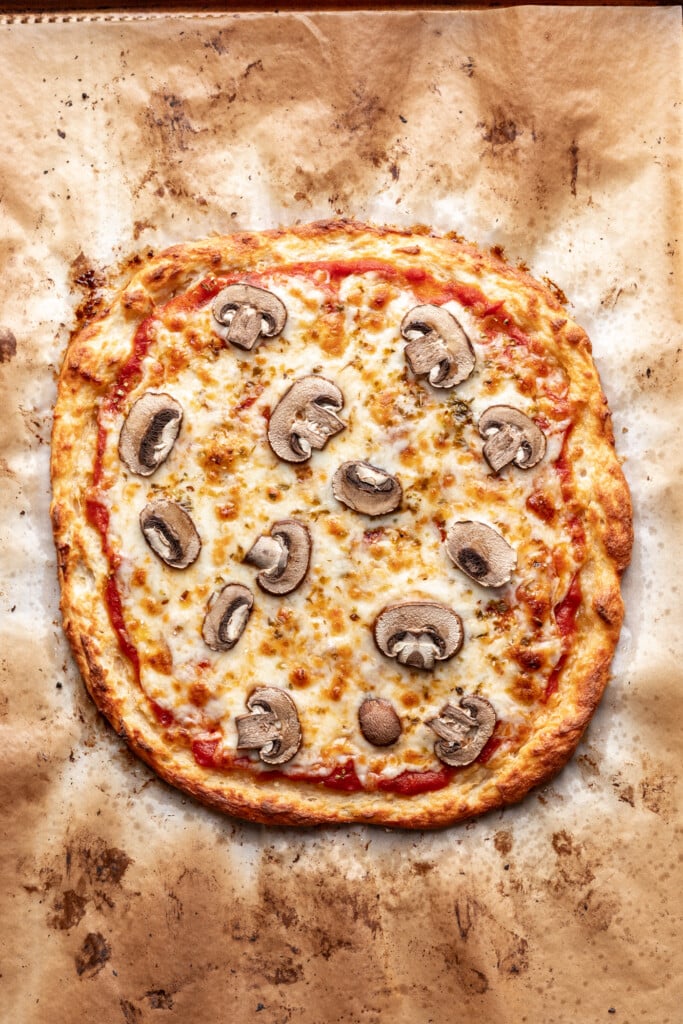 A pizza with mushrooms and cheese on a parchment paper