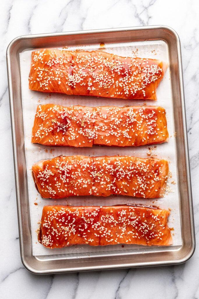4 pieces of salmon on a baking sheet with bbq sauce and sesame seeds