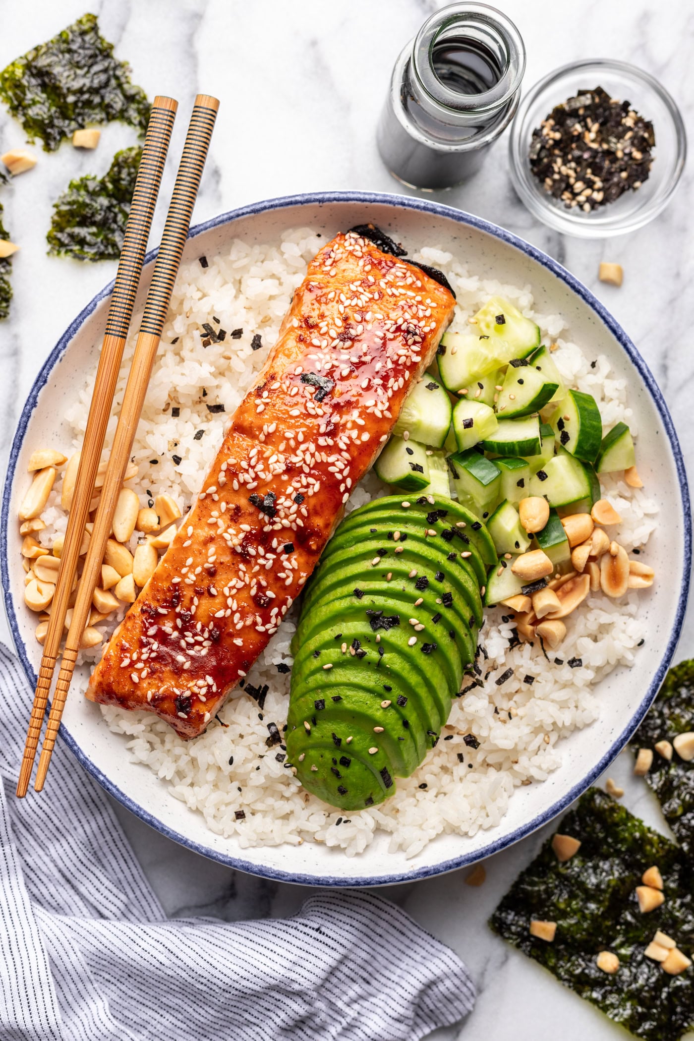 Salmon bowl with rice, cucumber, avocado, and seaweed on a white plate, garnished with sesame seeds.