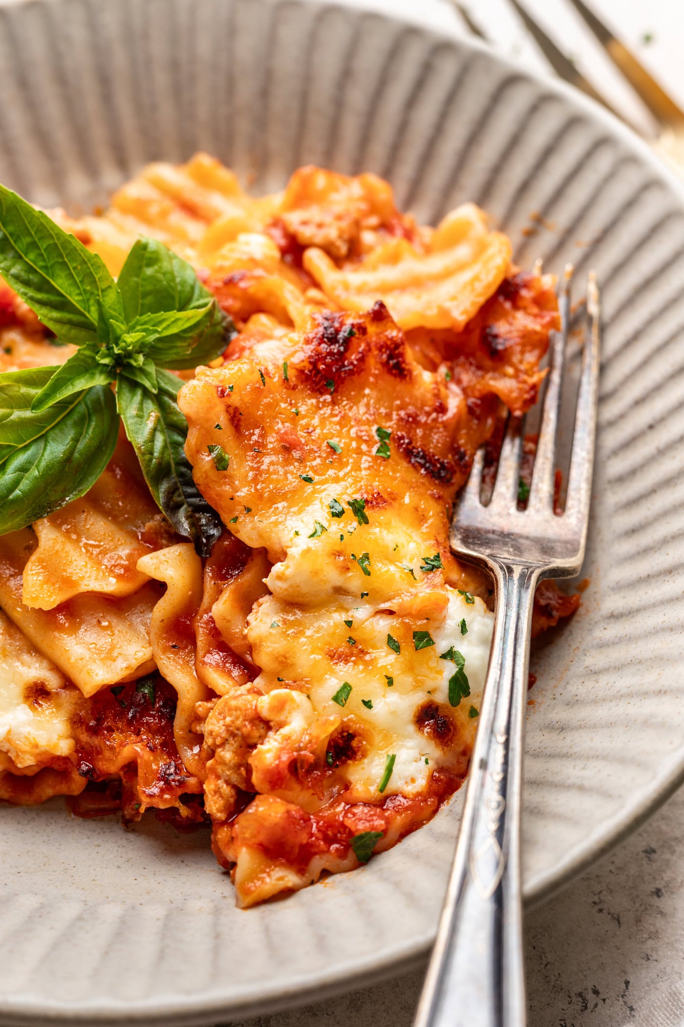 lasagna in a bowl with a fork and basil leaf