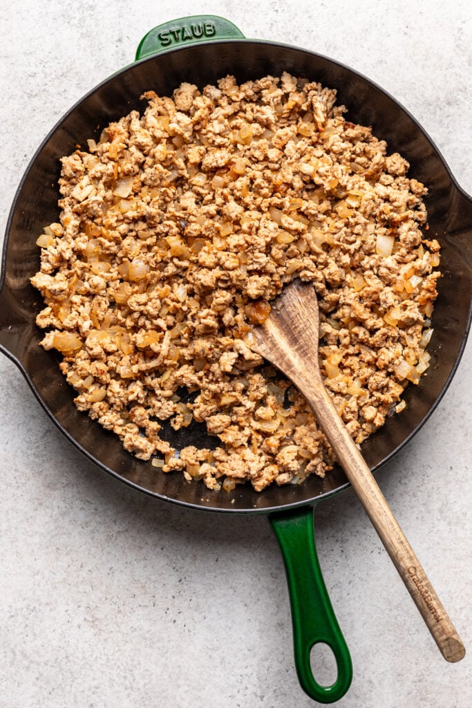 ground meat and onions in a skillet with a wooden spoone