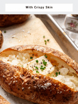A baked russet potato with crispy, salted skin is split open and topped with chopped chives, resting on a baking sheet with other potatoes. Text above reads Baked Russet Potato With Crispy Skin.