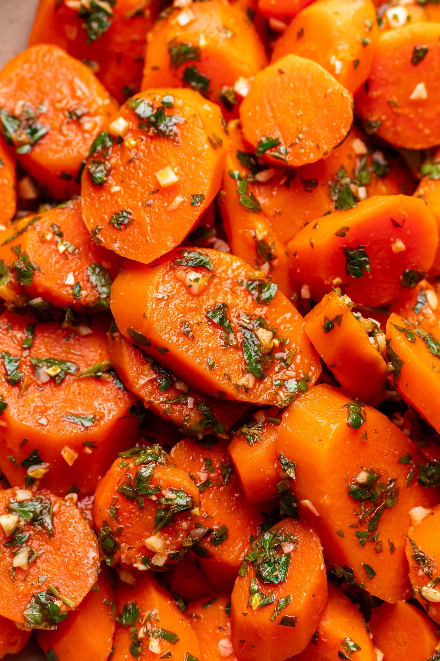Close-up of sliced cooked carrots garnished with chopped herbs and minced garlic, coated in a savory seasoning.