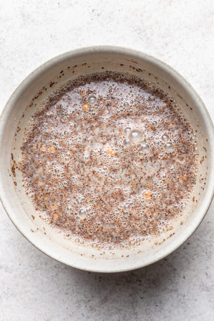 A ceramic bowl filled with a mixture of milk and chia seeds, creating a bubbly, slightly thick texture, on a light, textured surface.
